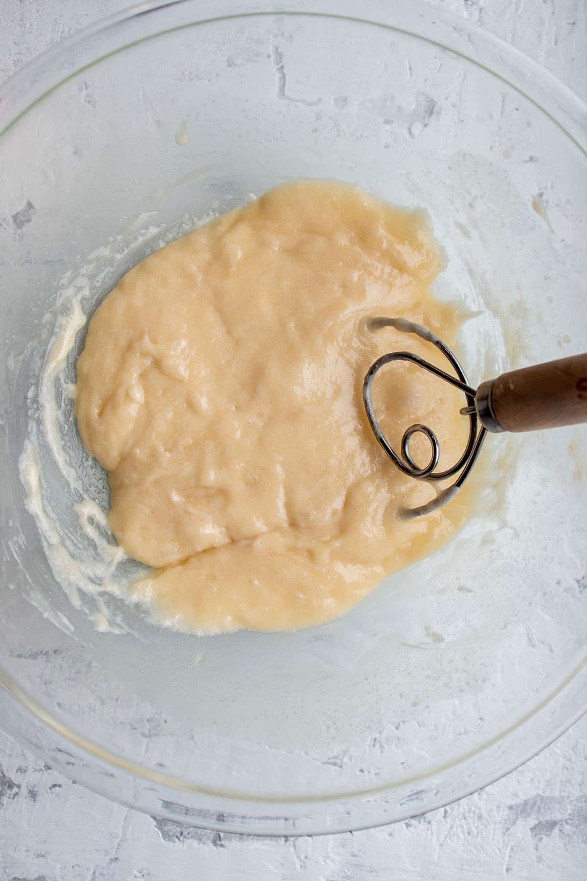 A glass bowl with a mix of sourdough starter butter, sugar being mixed together with a dough whisk.