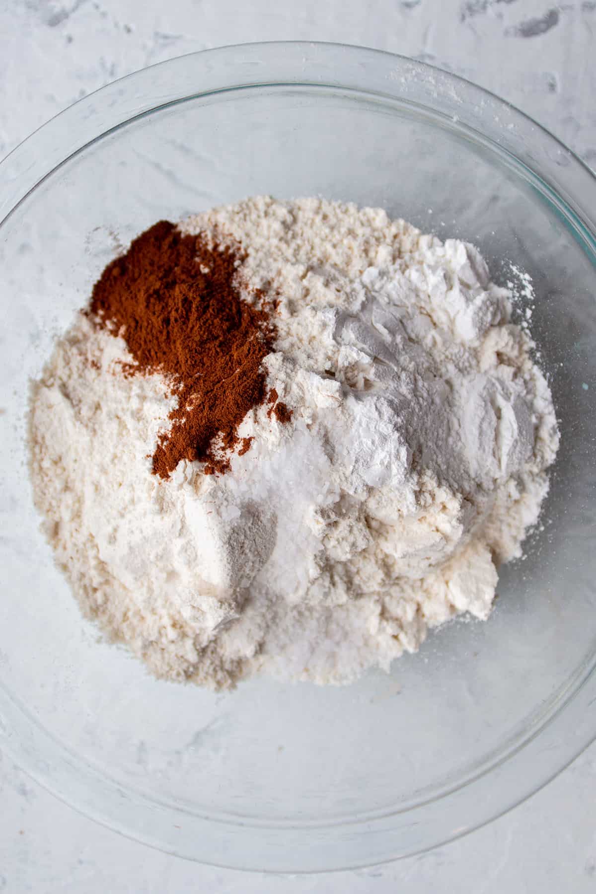 A glass bowl with flour, cinnamon, baking soda and salt.