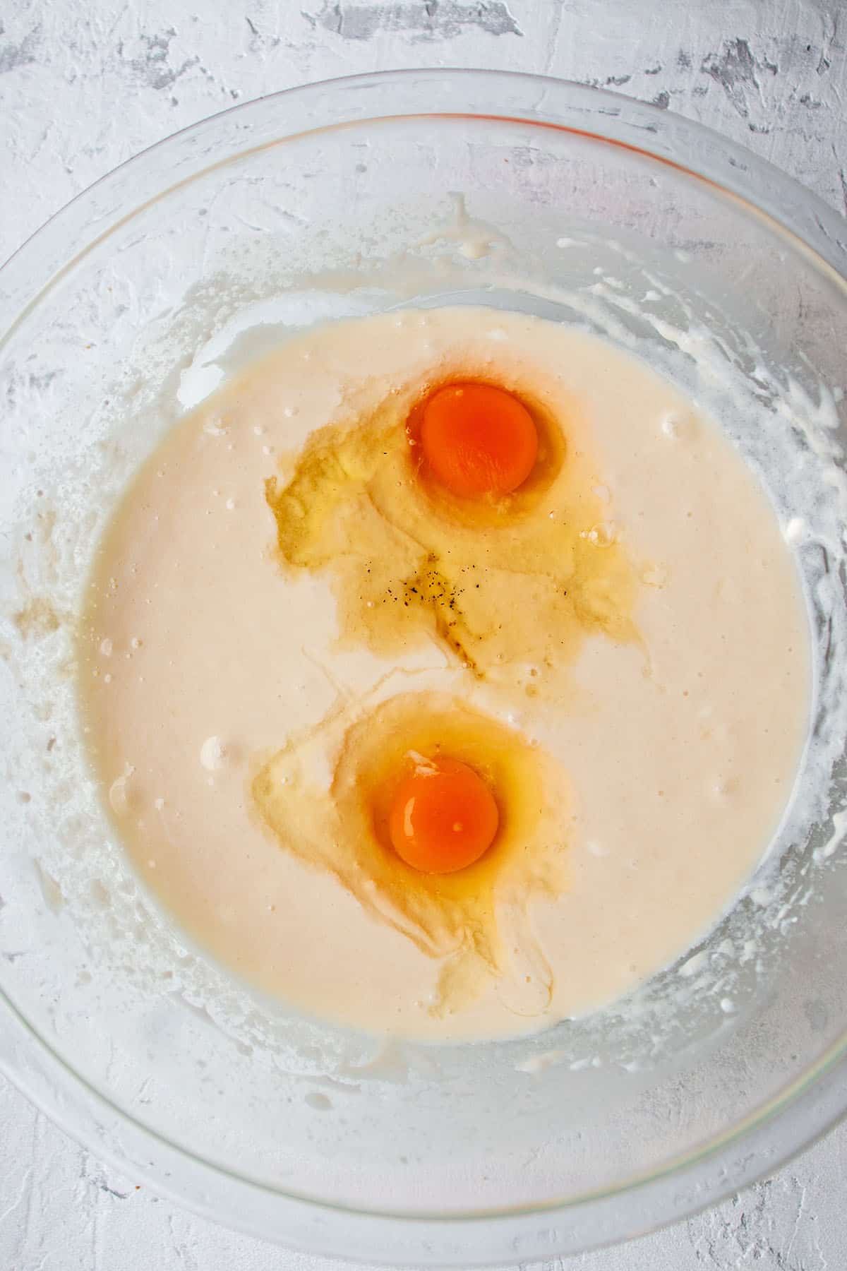 A glass bowl with a muffin batter with two eggs on top.