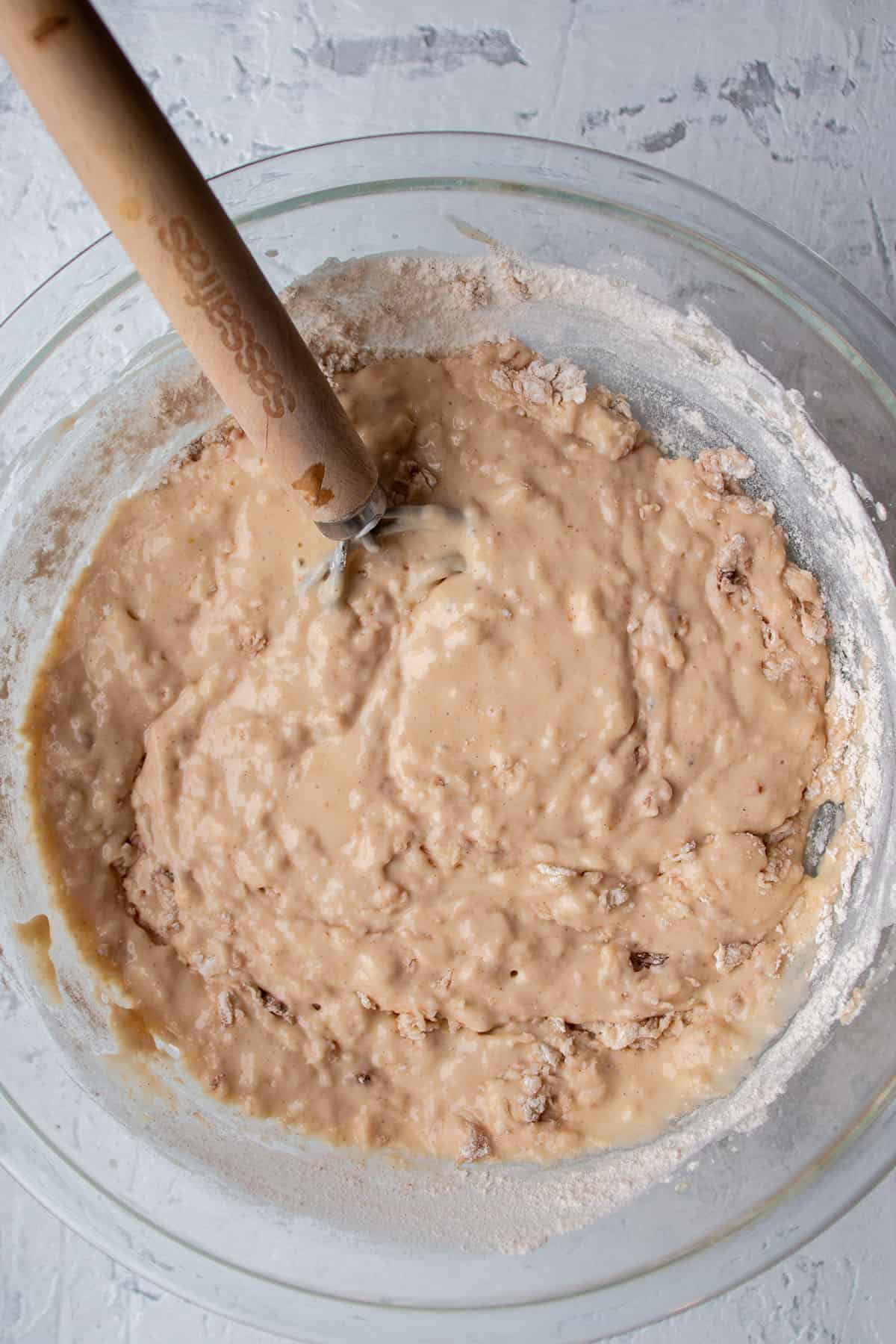 A glass bowl with a batter and a dough whisk mixing it up.