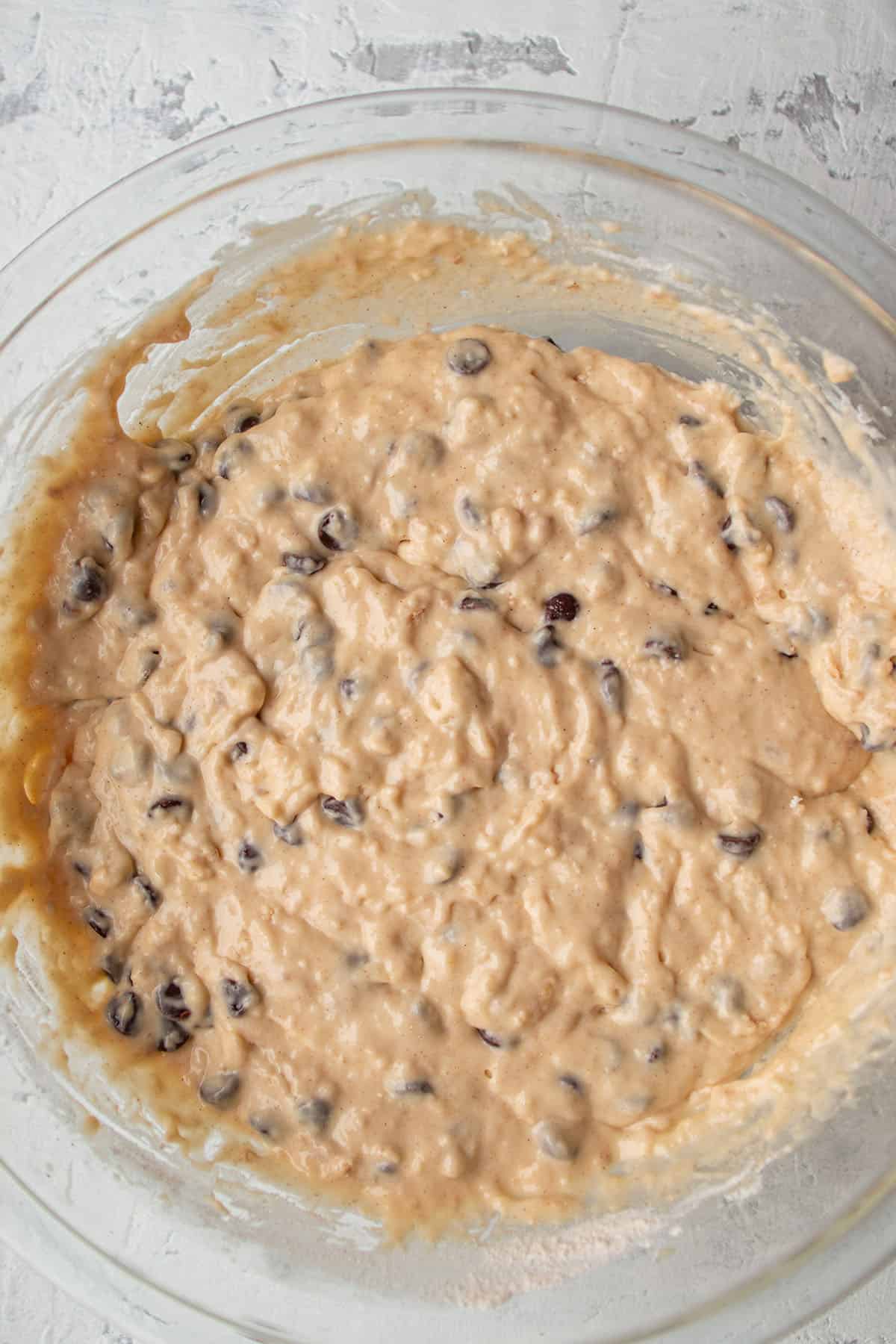 A large glass bowl with a batter that has chocolate chips inside.