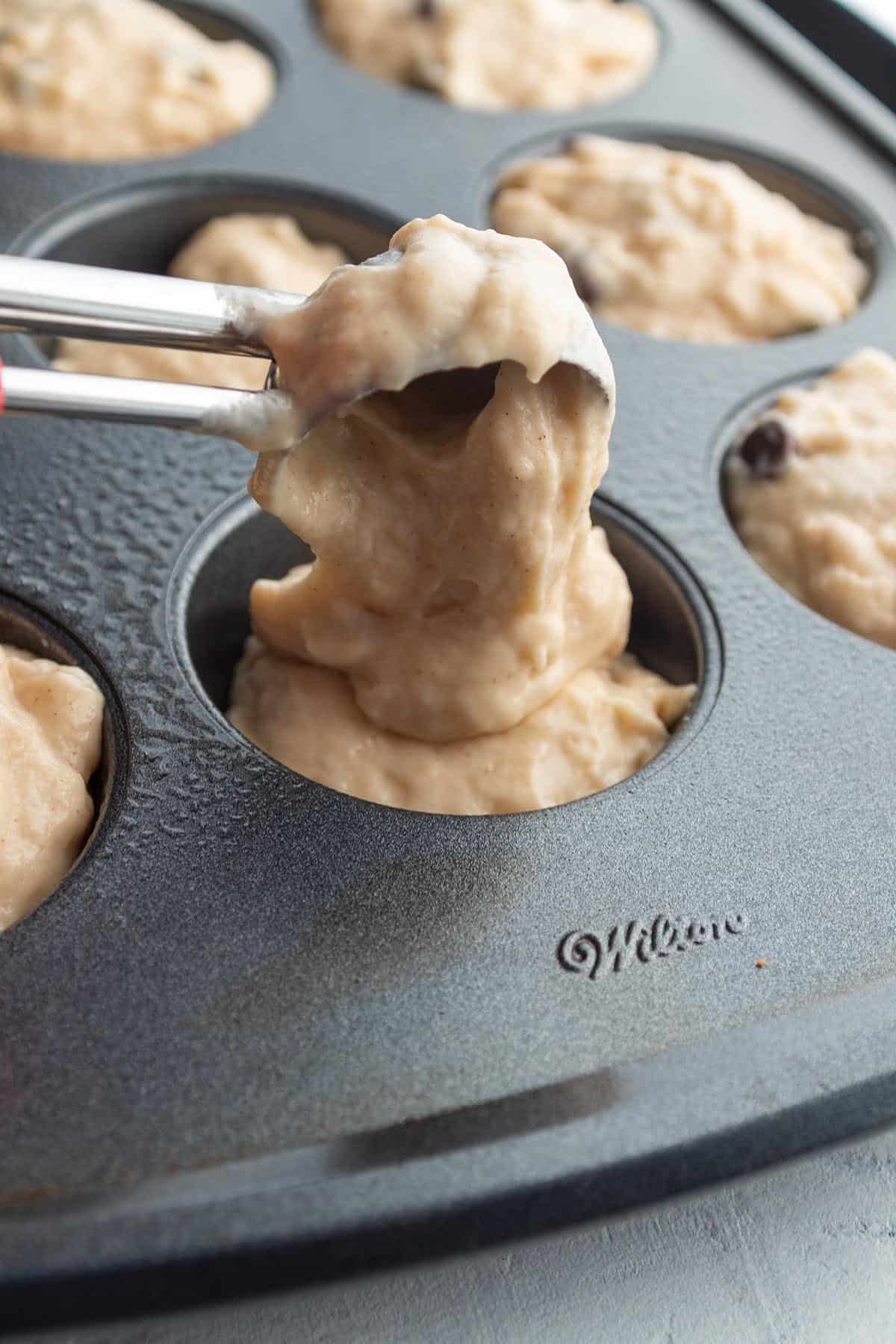 A cookie scoop dividing out muffin batter into a baking pan.