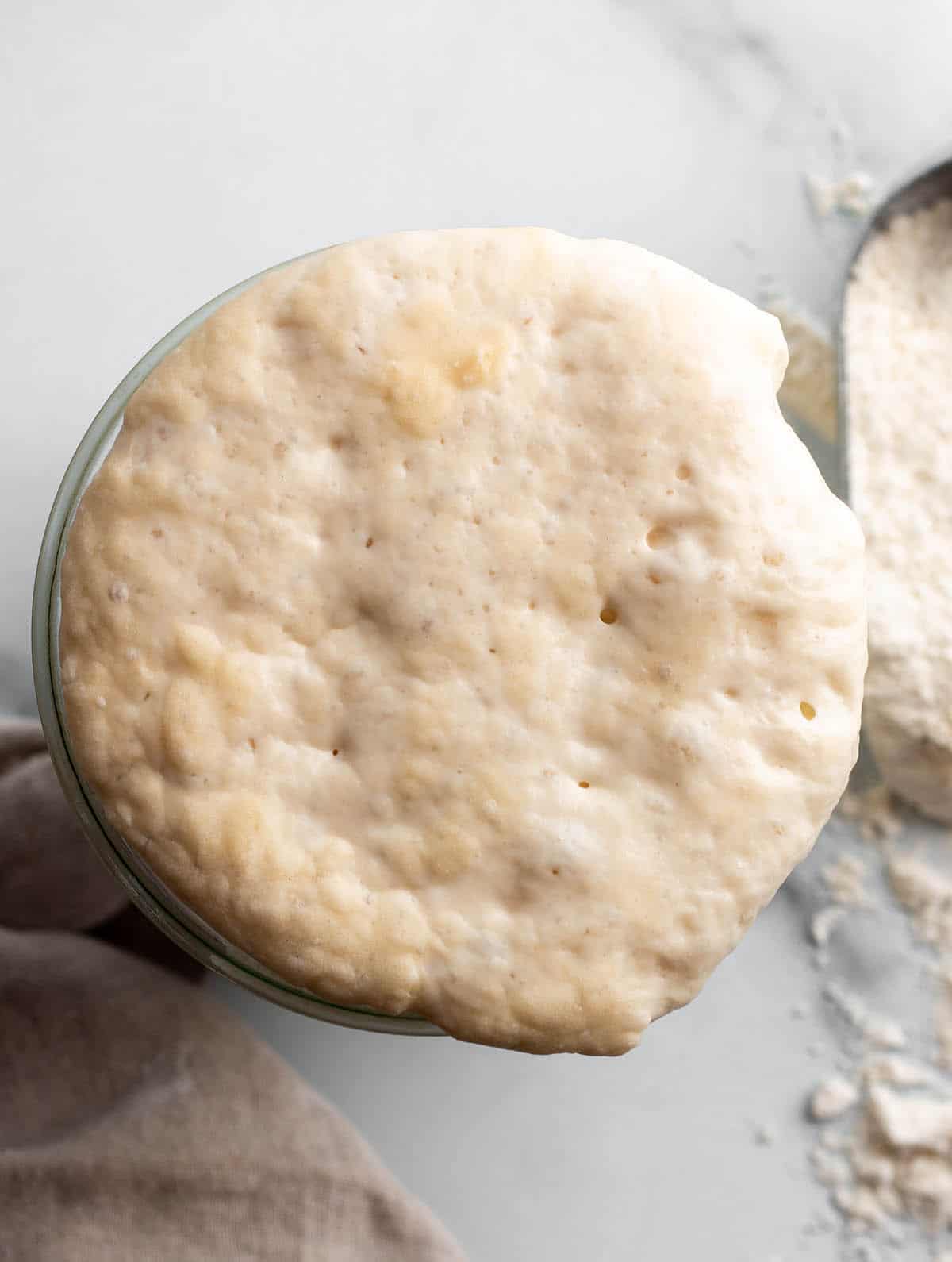 The overhead view of a sourdough starter growing over the top of a jar. 