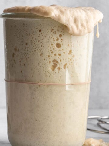 A tall jar with a sourdough starter pouring over the top.