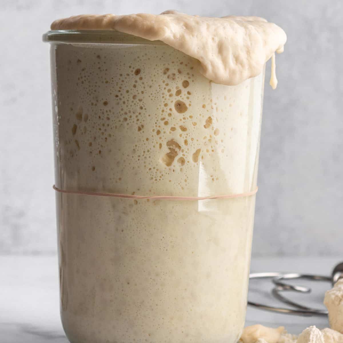 A tall jar with a sourdough starter pouring over the top.