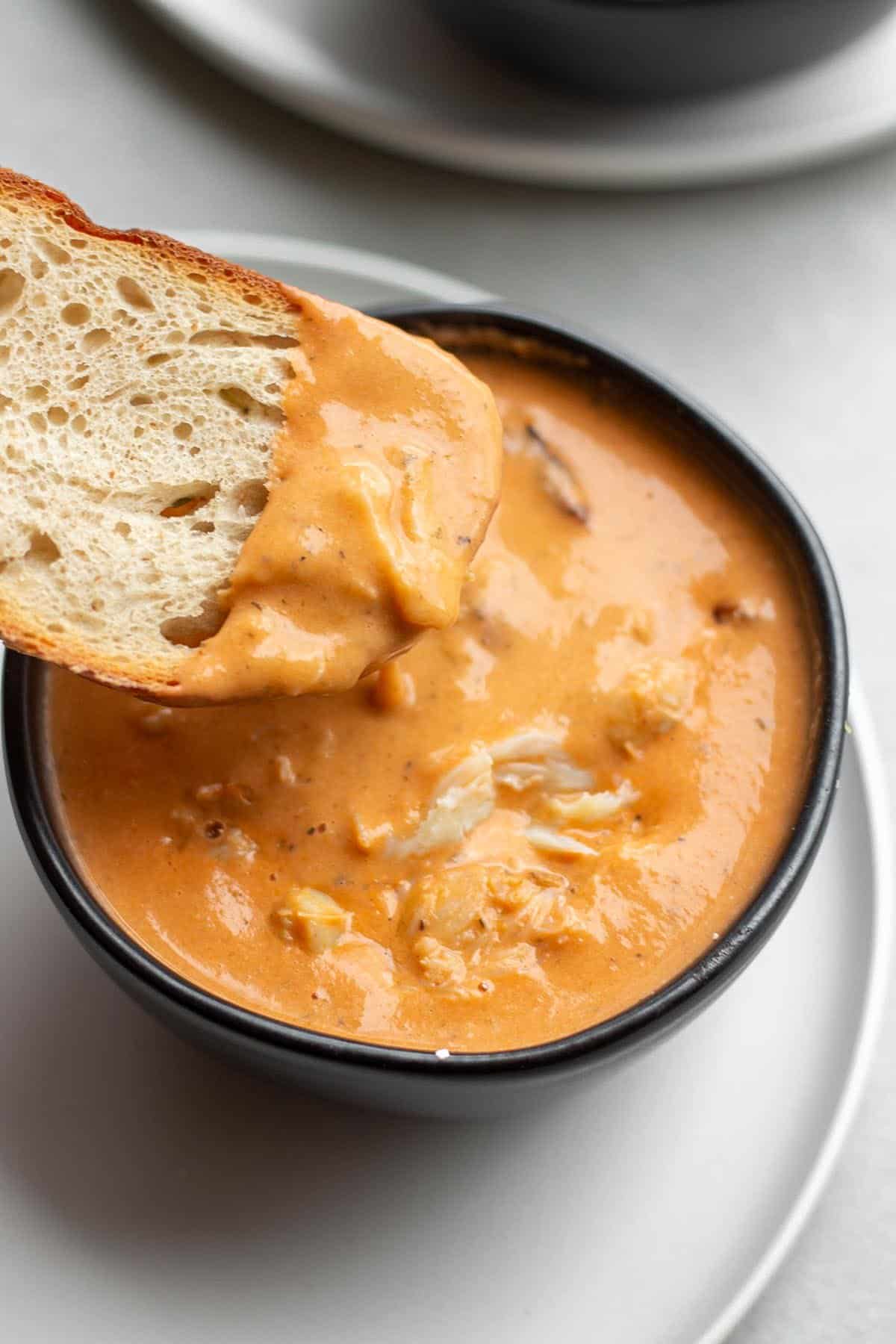 A black bowl with a crab bisque and a piece of sourdough scooping some out.