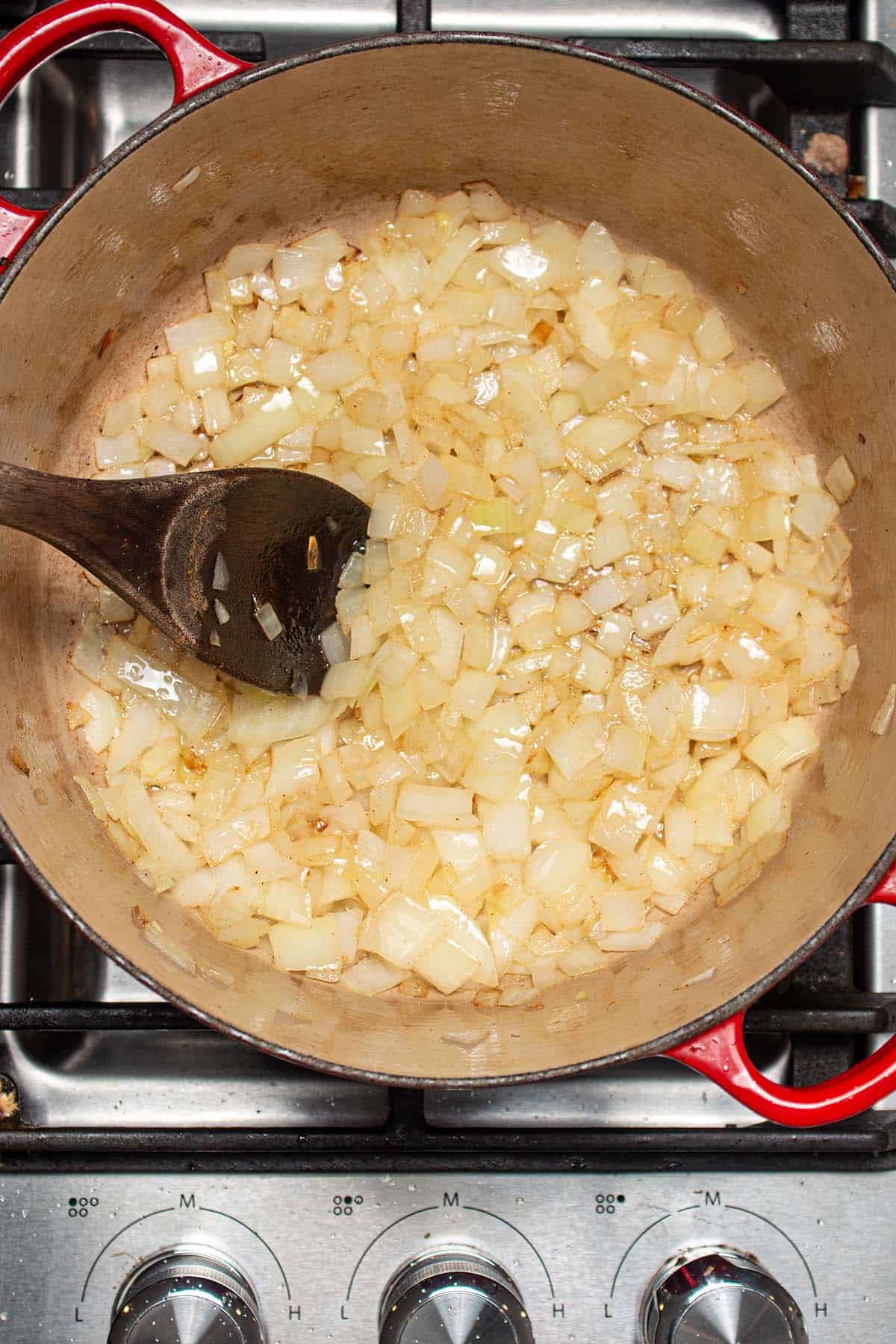 Onions sautéing in olive oil with a wooden spoon.