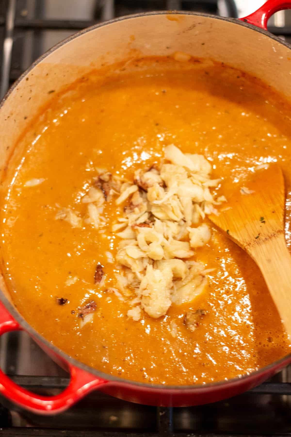 A creamy tomato soup with a pile of crab meat on top being stirred in.