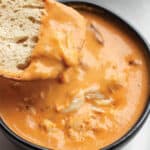 A bowl of crab bisque with a piece of sourdough scooping some out.