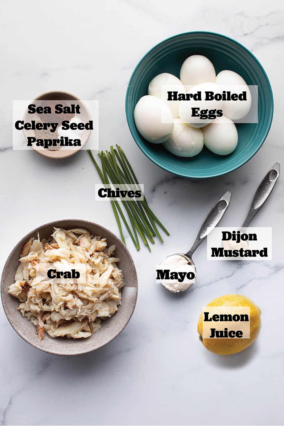 Ingredients to make deviled eggs. Hard boiled eggs, mayo, dijon, crab, lemon, celery seed, paprika, sea salt and fresh chives.