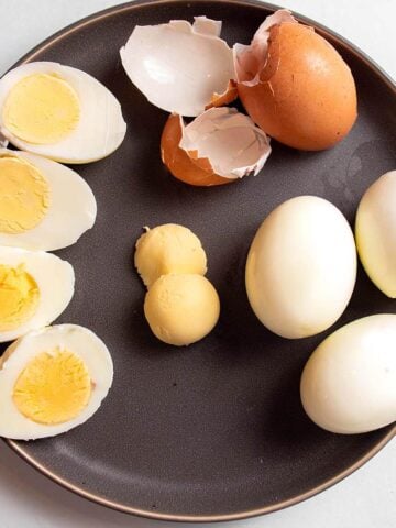 A plate with hard boiled eggs one peeled, one cut in half and one with the yolks removed.
