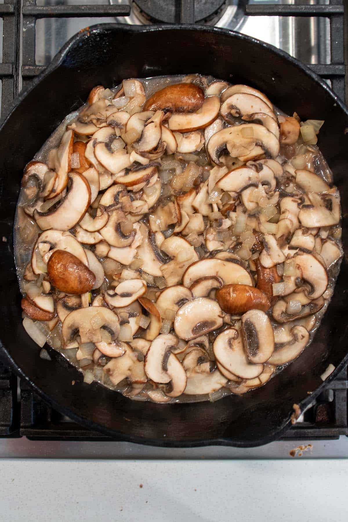 A cast iron skillet with mushrooms being sautéed in butter.
