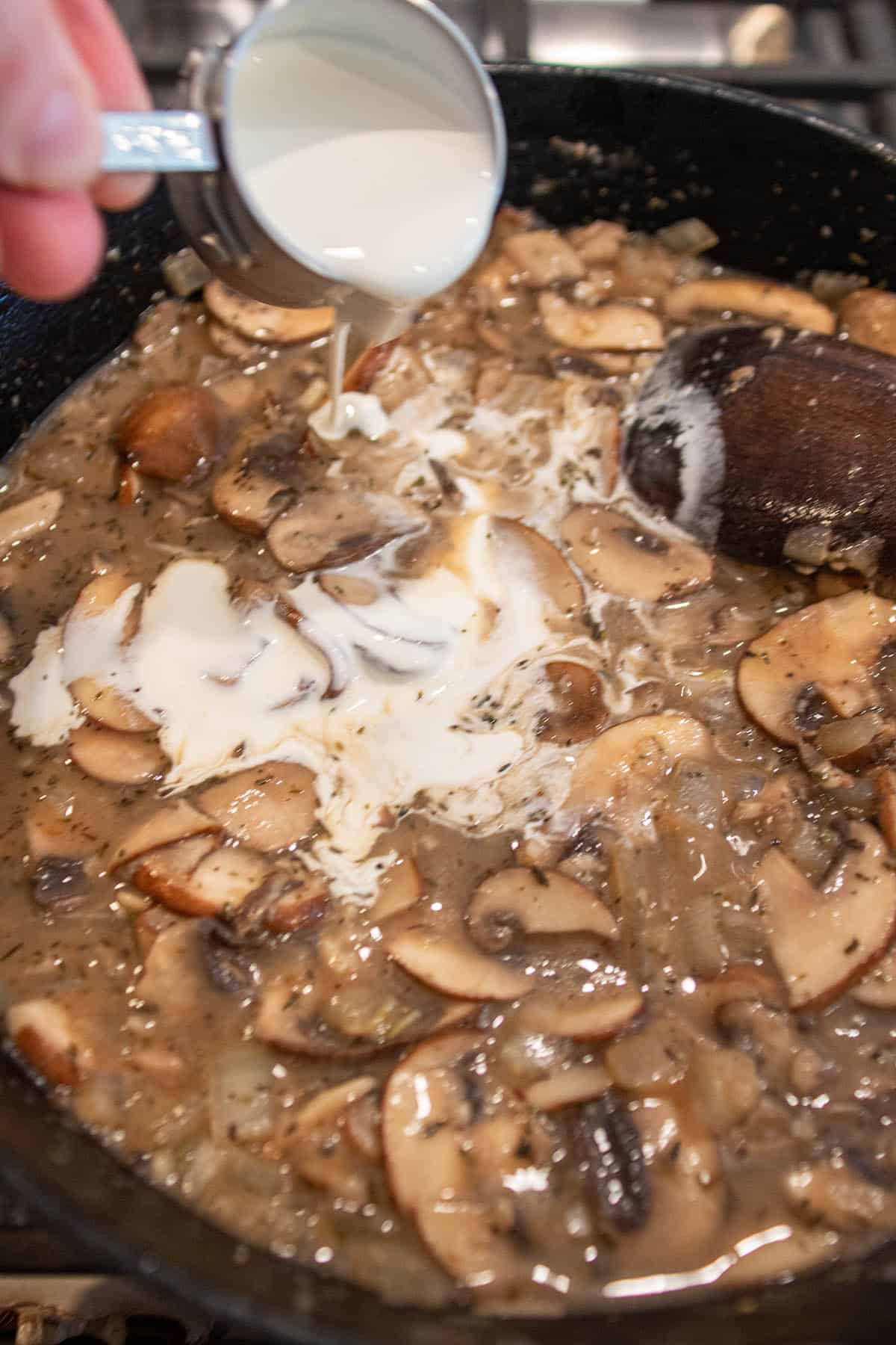 A cast iron skillet with cooked mushrooms and cream being poured in.