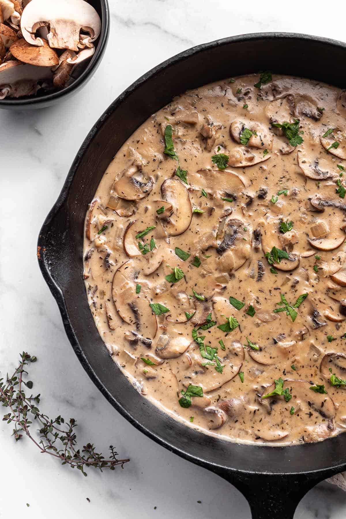 A cast iron skillet with a mushroom sauce and fresh parsley on top.