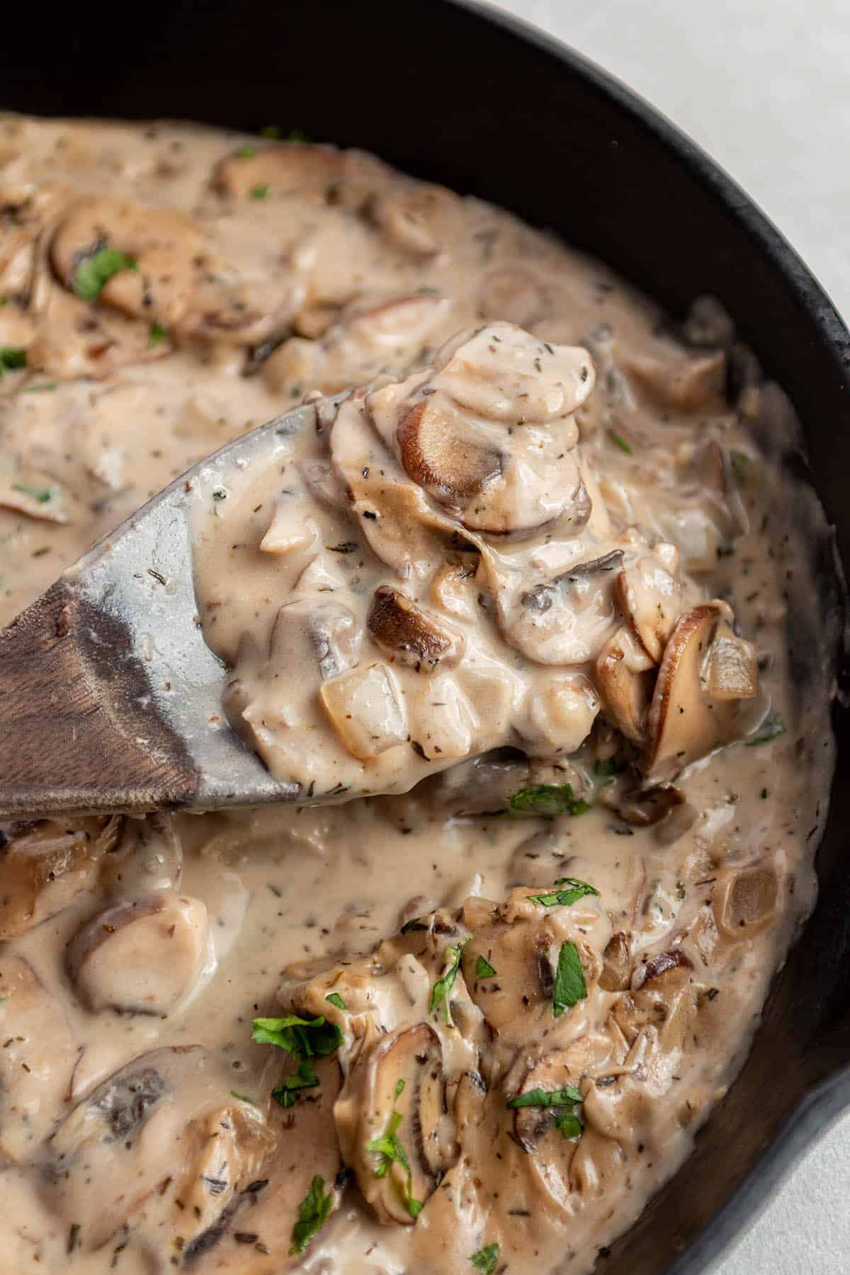 A cast iron skillet with a mushroom sauce and a wooden spoon scooping some out.