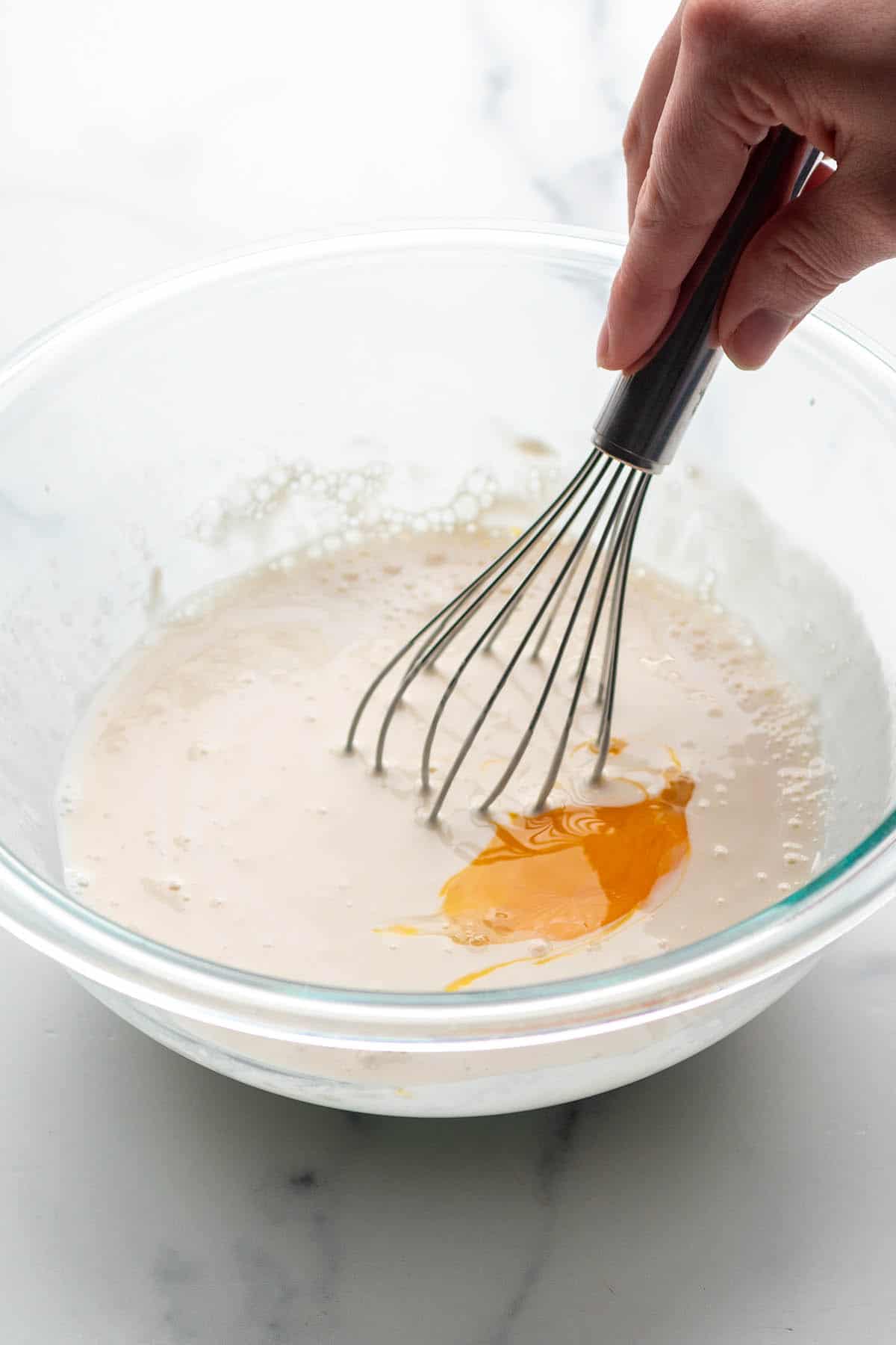 A glass bowl with a whisk stirring waffle batter.
