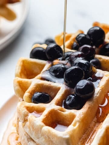 A stack of sourdough waffles with blueberries and syrup.