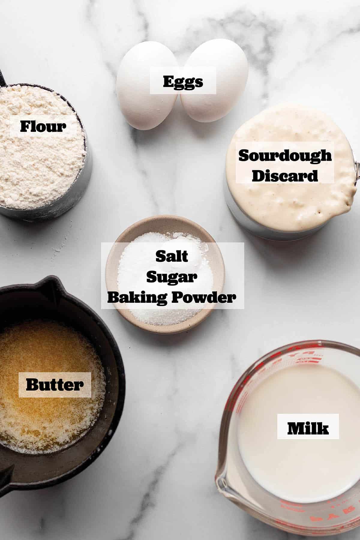 Ingredients to make waffles. Flour, eggs, sourdough starter, milk butter, baking powder, sugar and salt.
