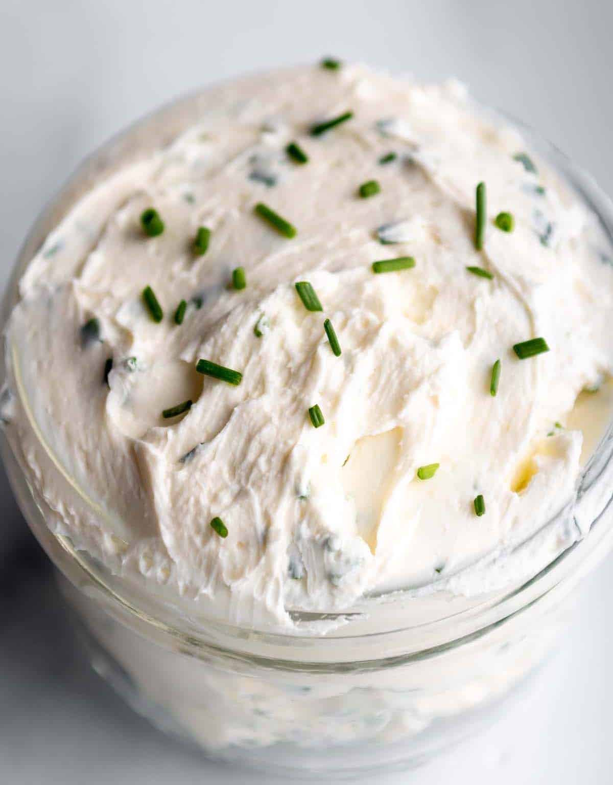 A jar with whipped cream cheese and chives. 