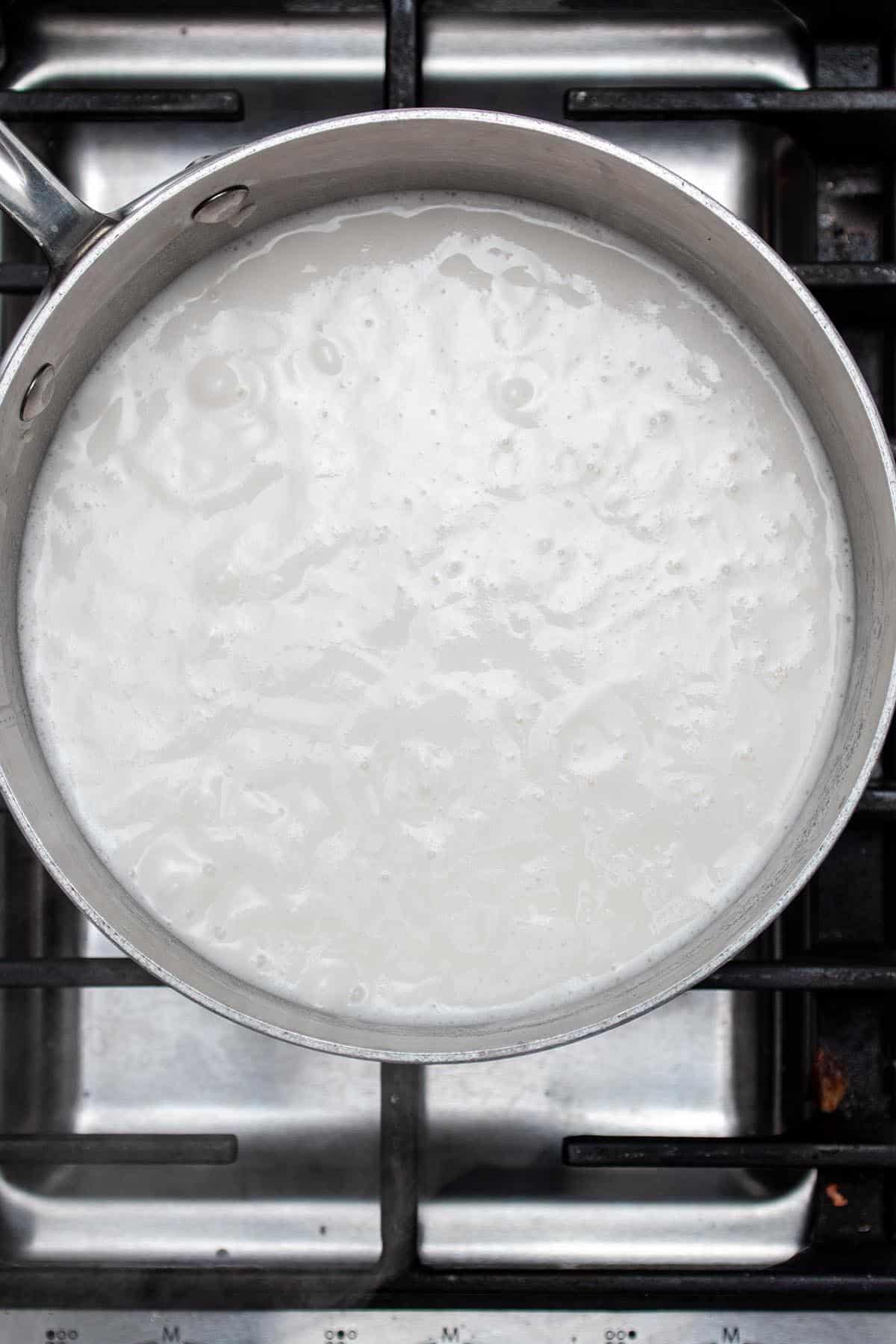 A small pot with rice simmering in a milk and water mix on a stove.