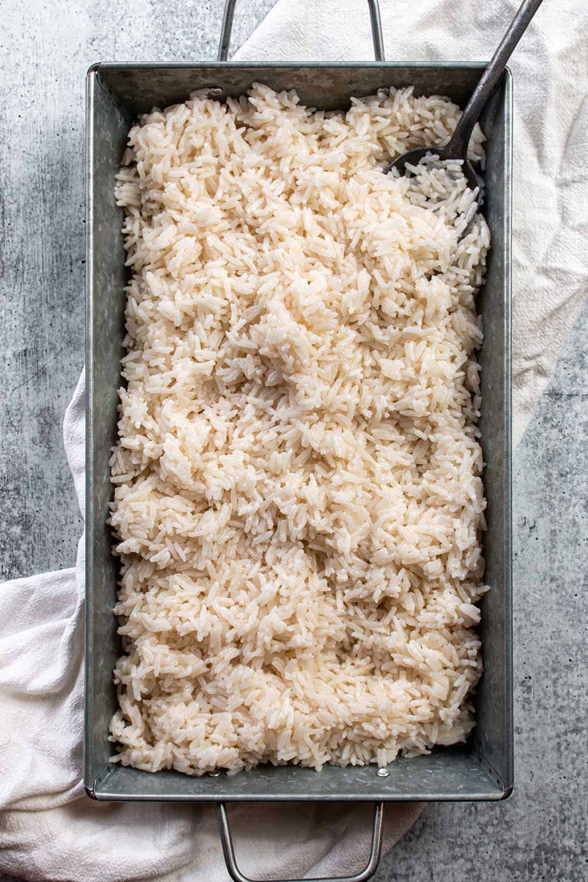 A metal tray with a pile of coconut rice and a metal slotted spoon.