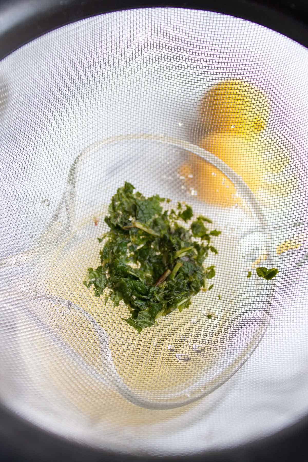 Mint being strained out through a fine mesh strainer.