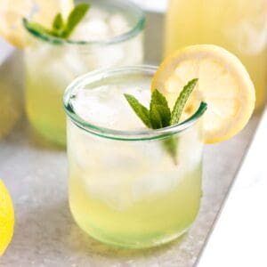 A glass of lemonade with a fresh lemon and mint.