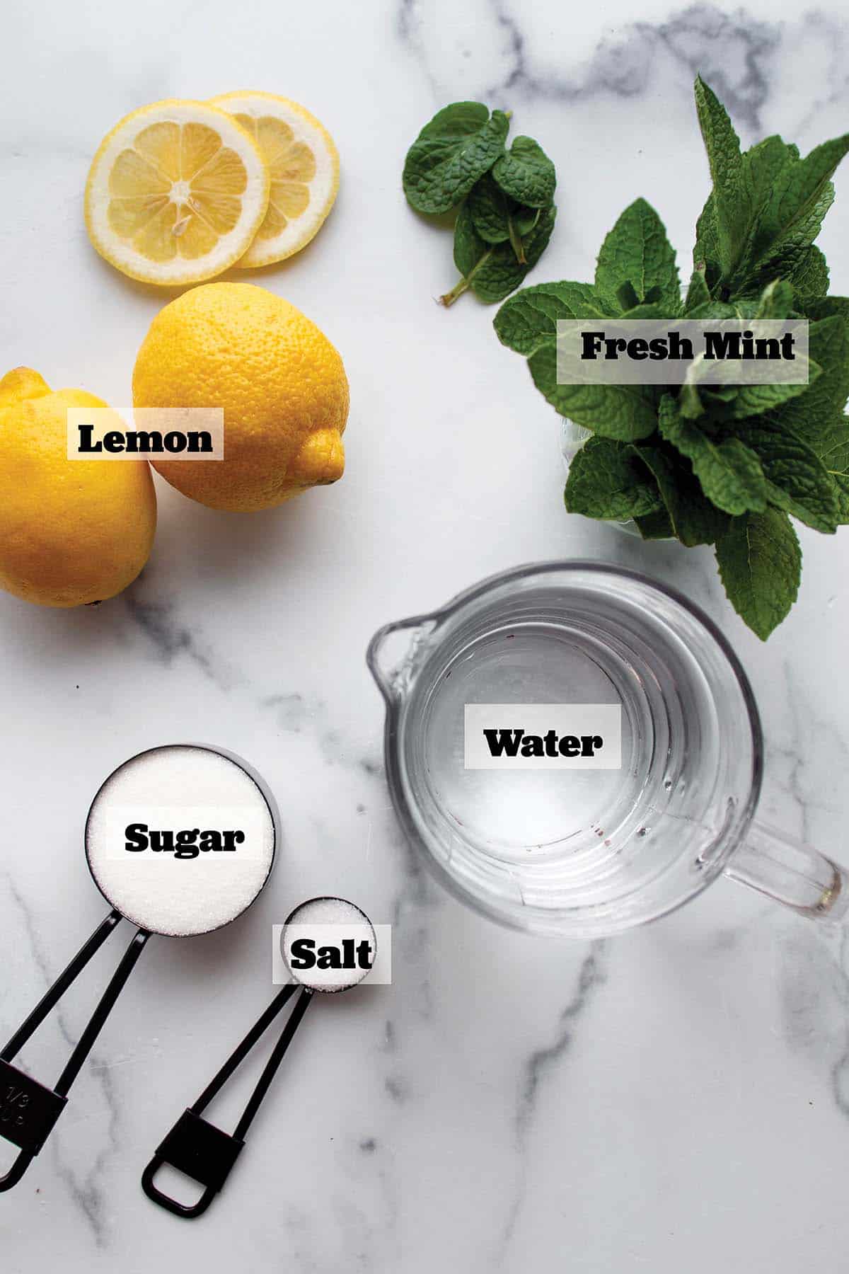 Fresh lemon, mint, a cup of water and measuring spoons with sugar and salt.