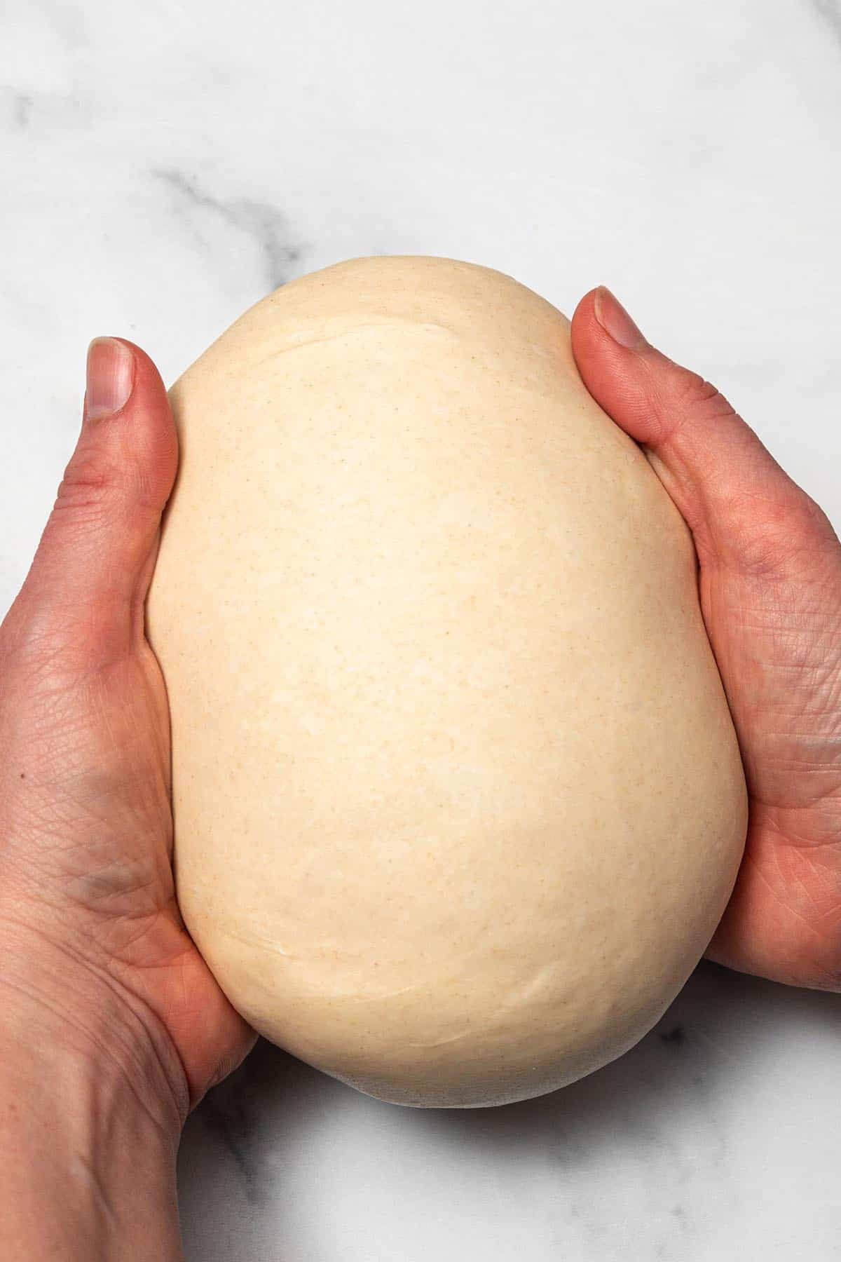 Two hands forming ball of dough.
