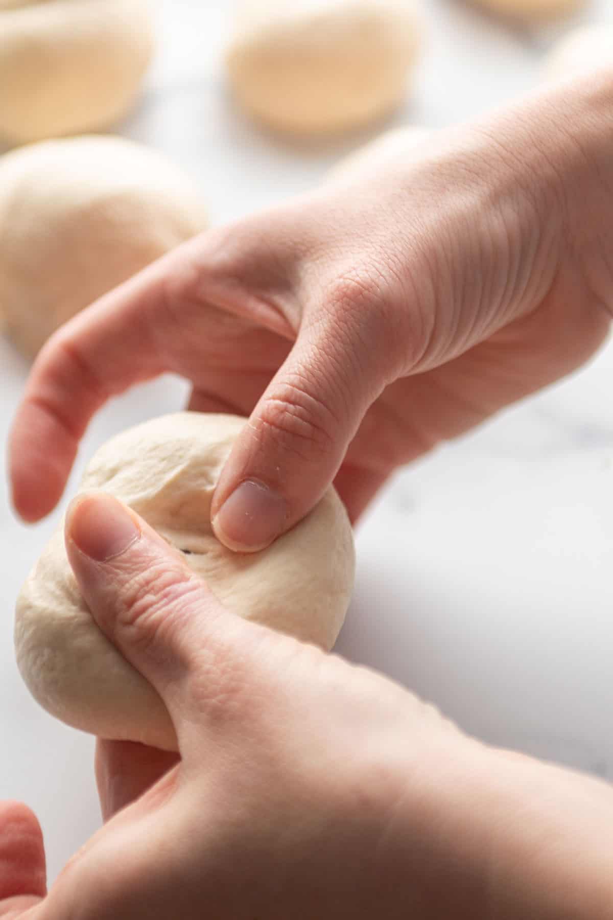 Two hands poking a hole in a small ball of dough.