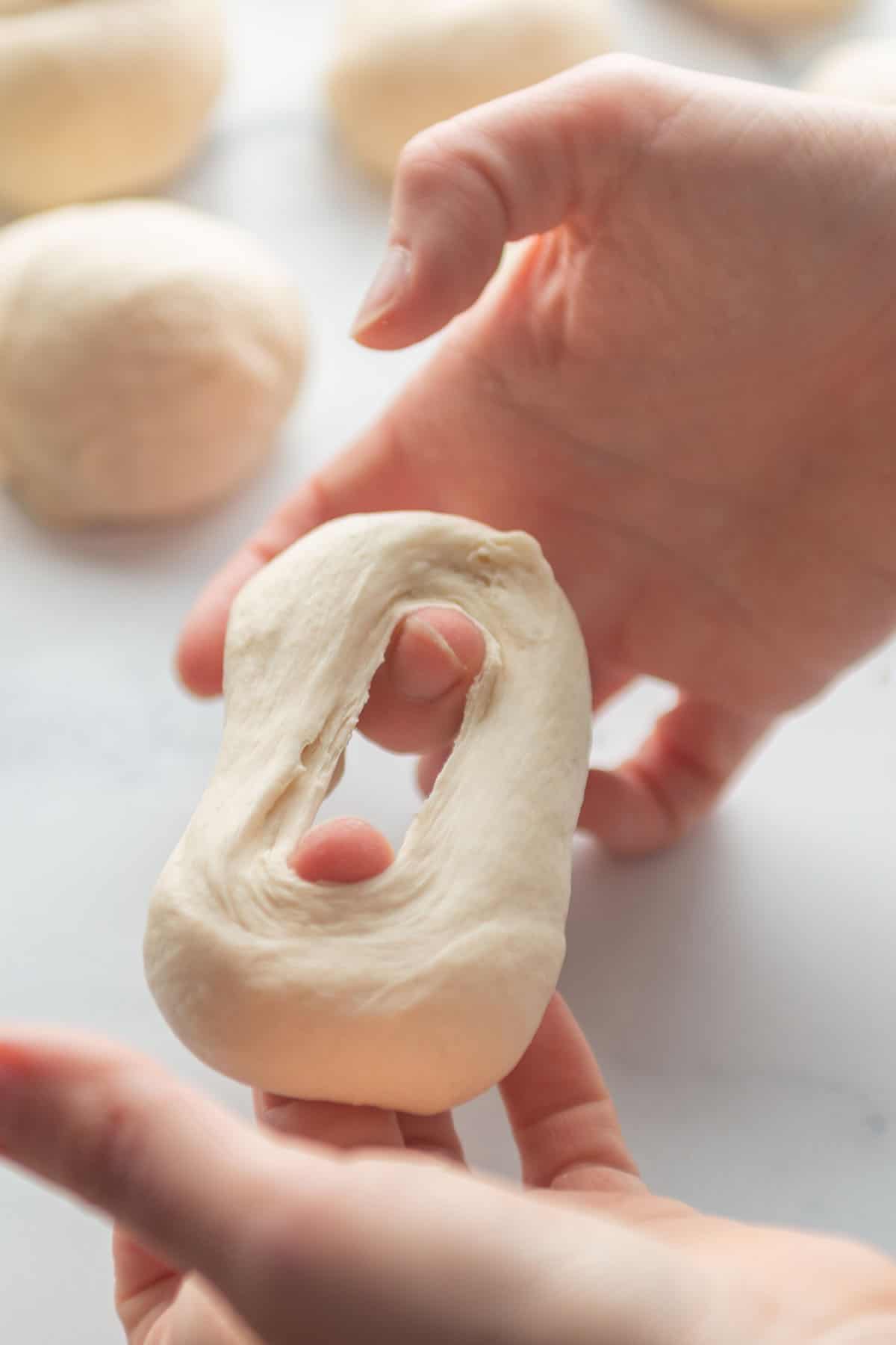 Two hands forming a ball of dough into a ring.