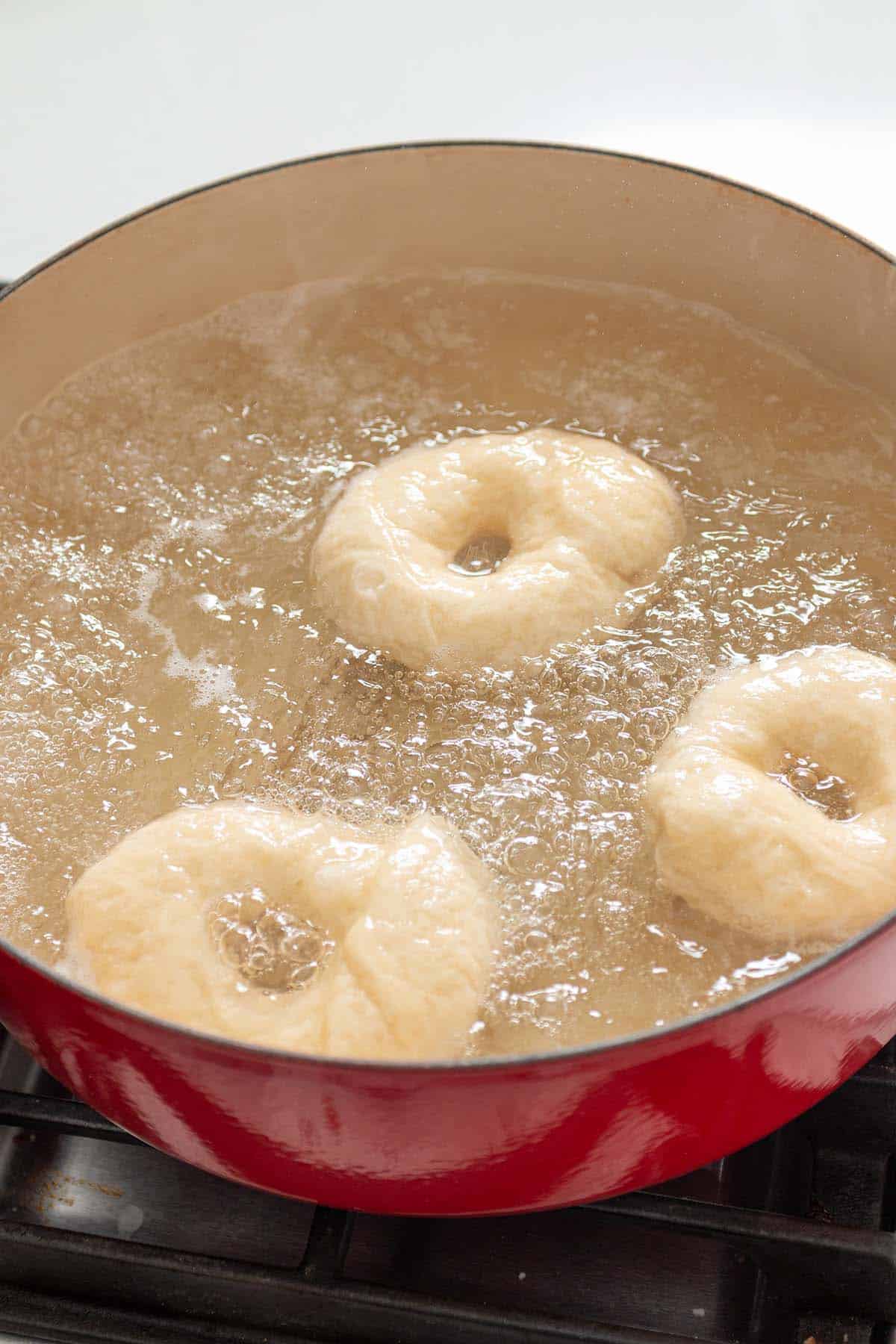 A large dutch oven with boiling water and bagels floating.