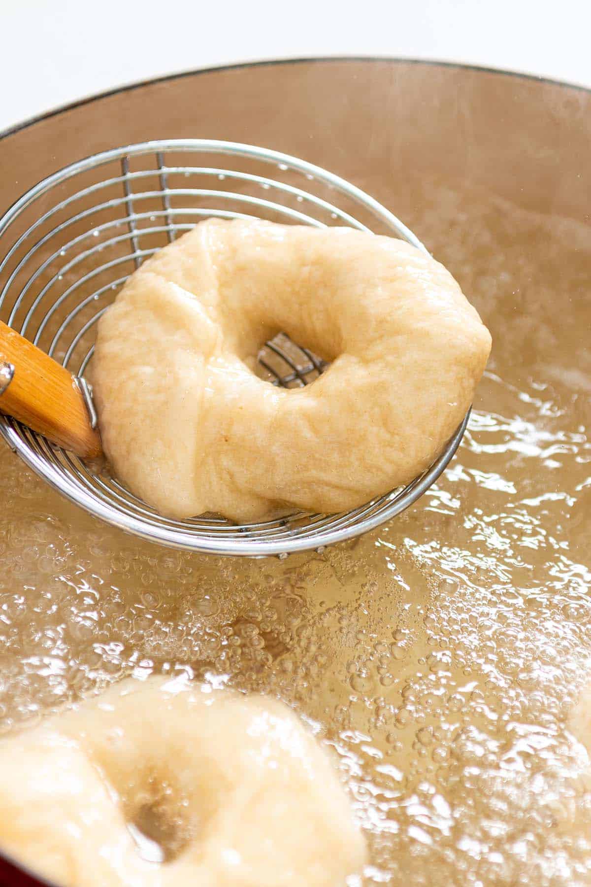 A skimmer scooping out a bagel from boiling water.