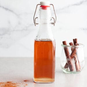 A flip lock bottle with a brown simple syrup and cinnamon sticks in the back.