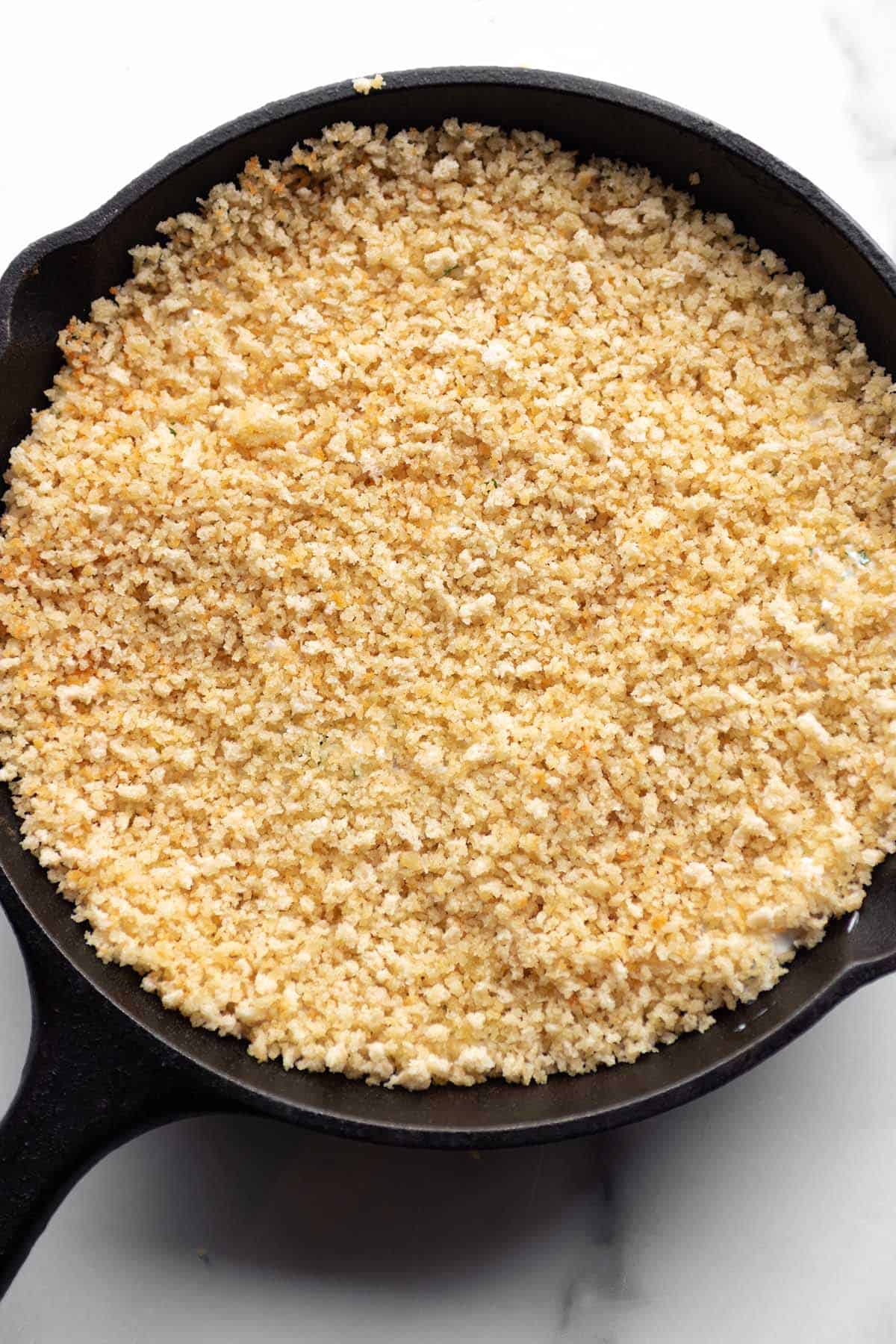 A cast iron pan with a dip and panko crumbs spread over the top.