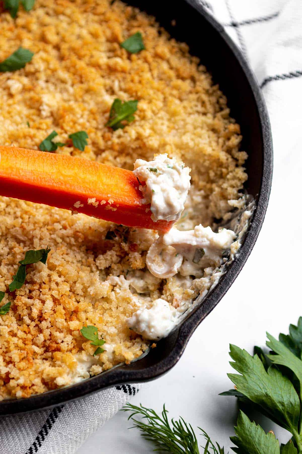 A carrot scooping out some clam dip from a small pan.
