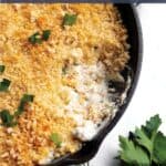 A cast iron pan with a clam dip and panko crumbs on top with fresh herbs.