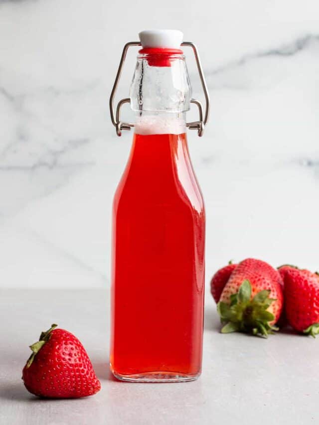 A glass flip lock bottle with a strawberry simple syrup and fresh strawberries.