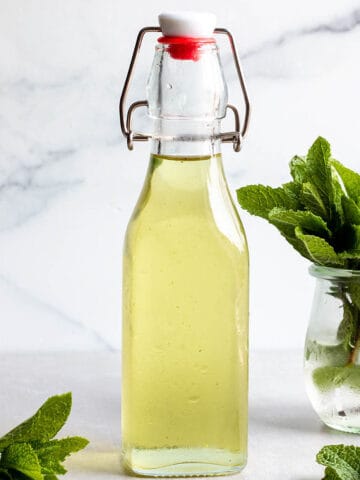 A glass flip lock bottle with a green simple syrup and fresh mint leaves.
