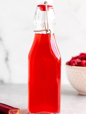 A glass flip lock bottle with a rhubarb simple syrup and fresh rhubarb.