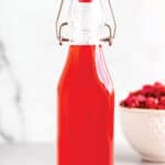 A glass bottle with a red liquid and bowl of diced rhubarb in the back.
