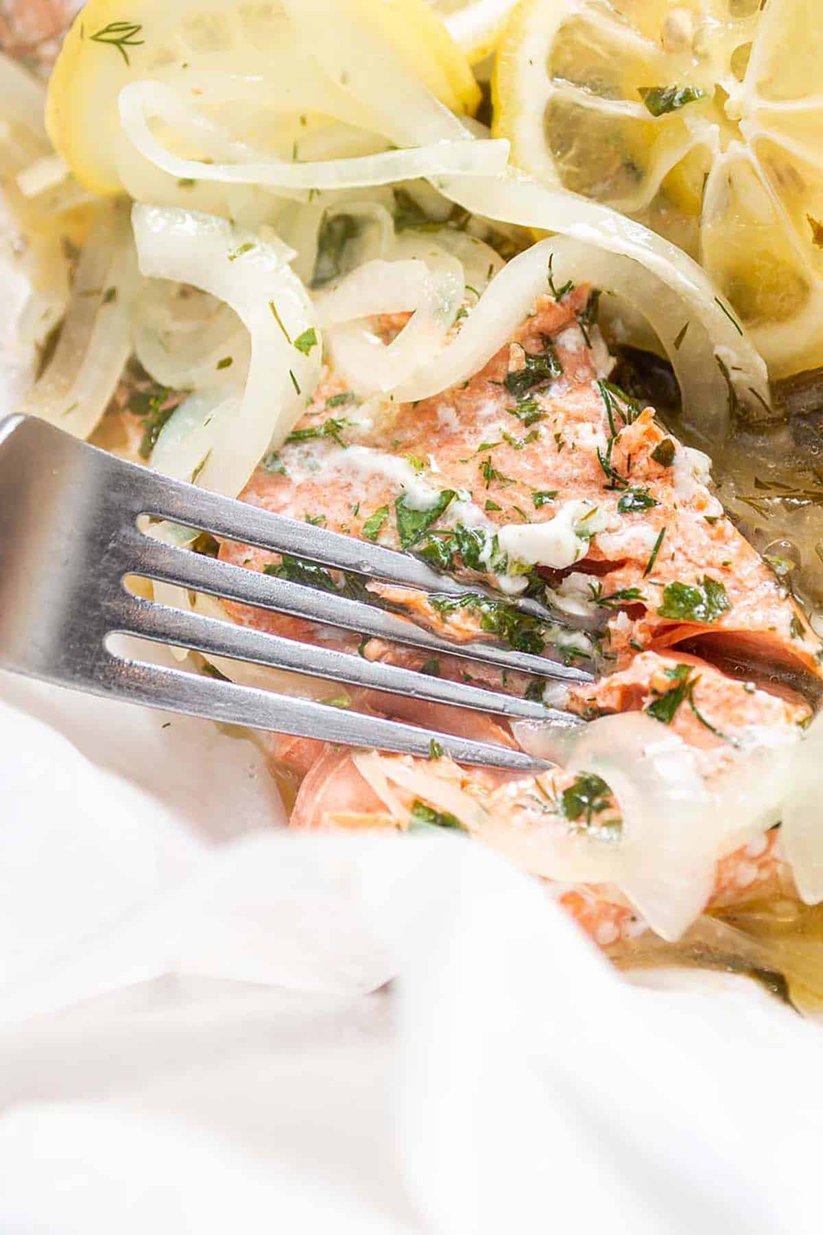 a fork cutting into a fresh salmon filet made with lemon and herb and onions.