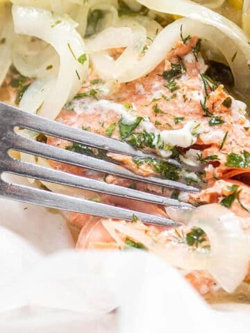 A filet of salmon being cut with a fork and fresh lemon slices.