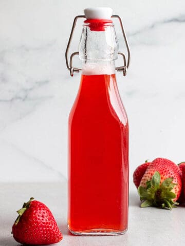 A glass flip lock bottle with a strawberry simple syrup and fresh strawberries.