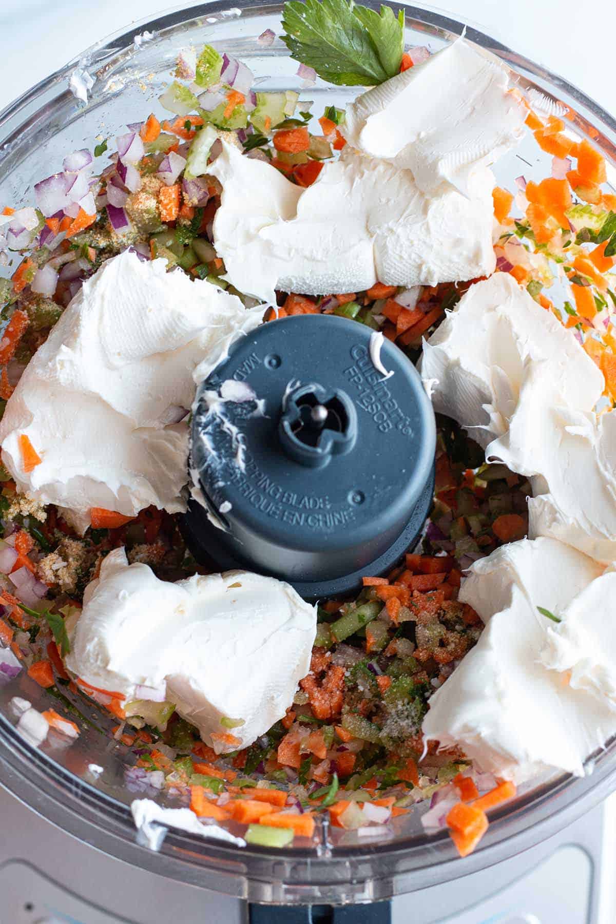 A food processor with finely diced veggies and clumps of cream cheese.