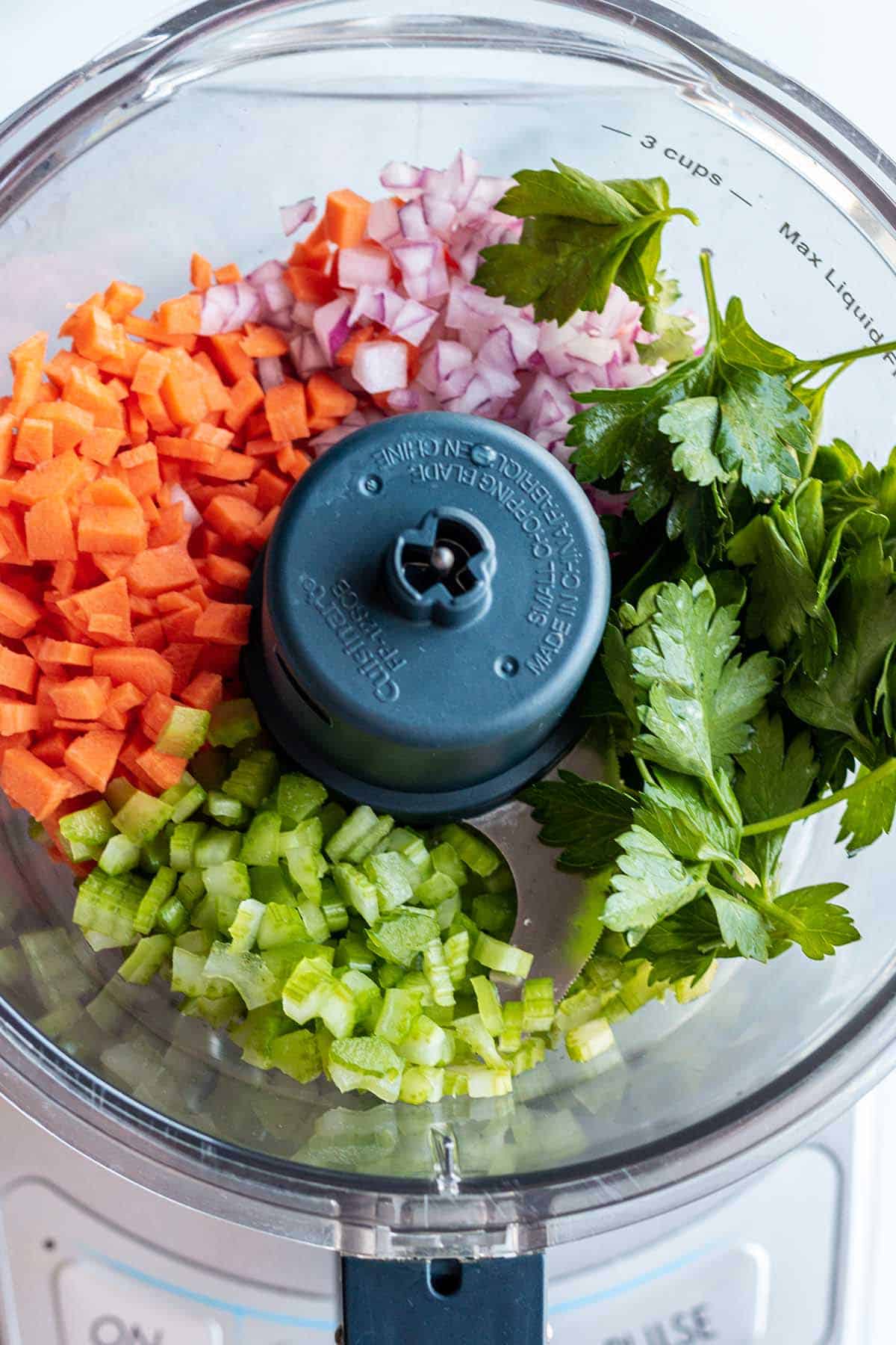A food processor with diced carrots, celery, parsley and red onion