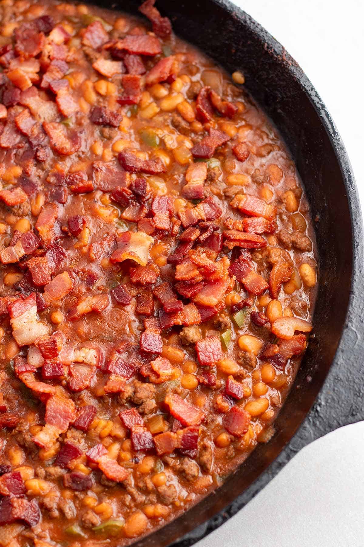 A cast iron pan with a baked bean mix topped with crispy bacon.