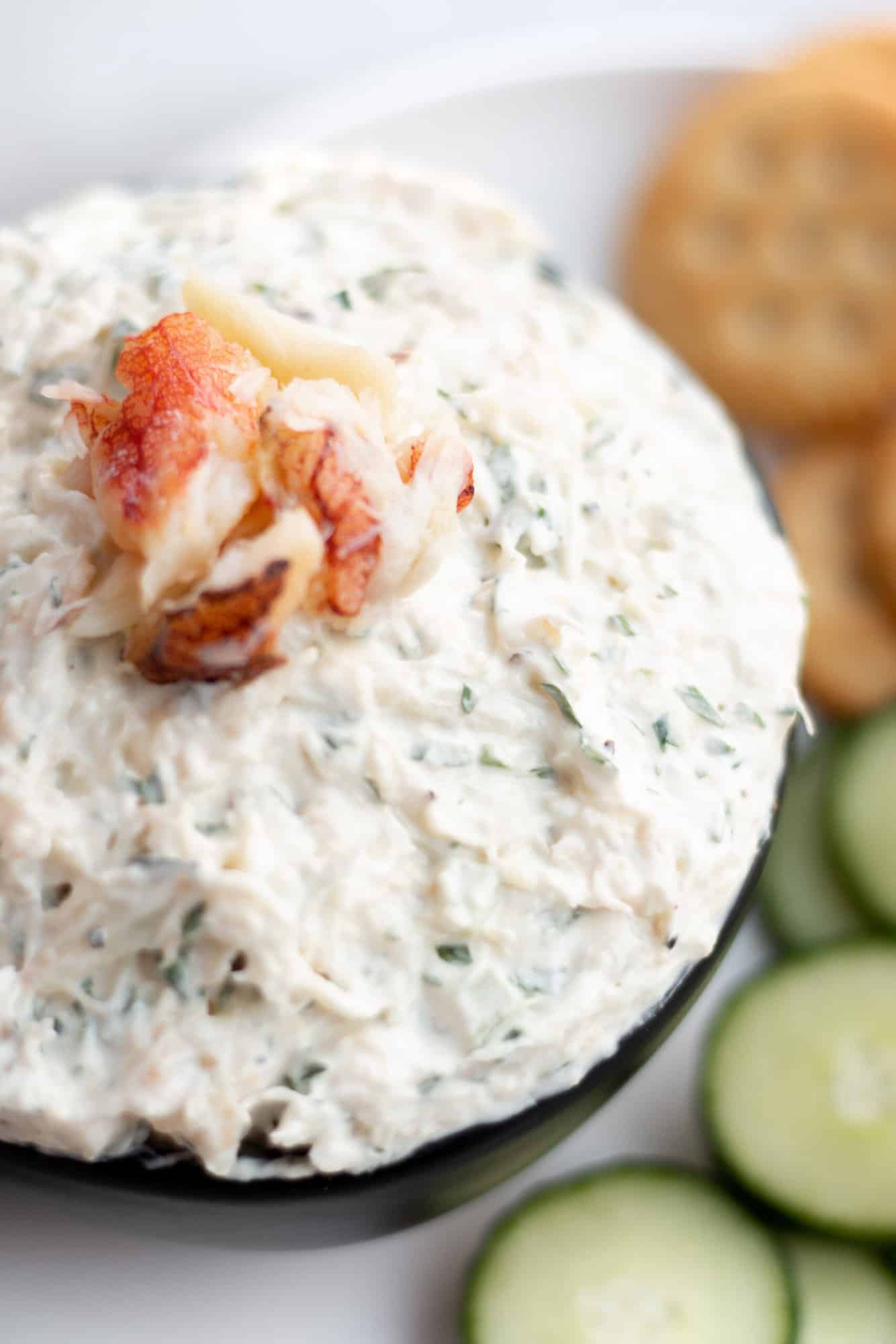 A plate with a bowl of fresh crab dip, ritz and cucumber slices. 