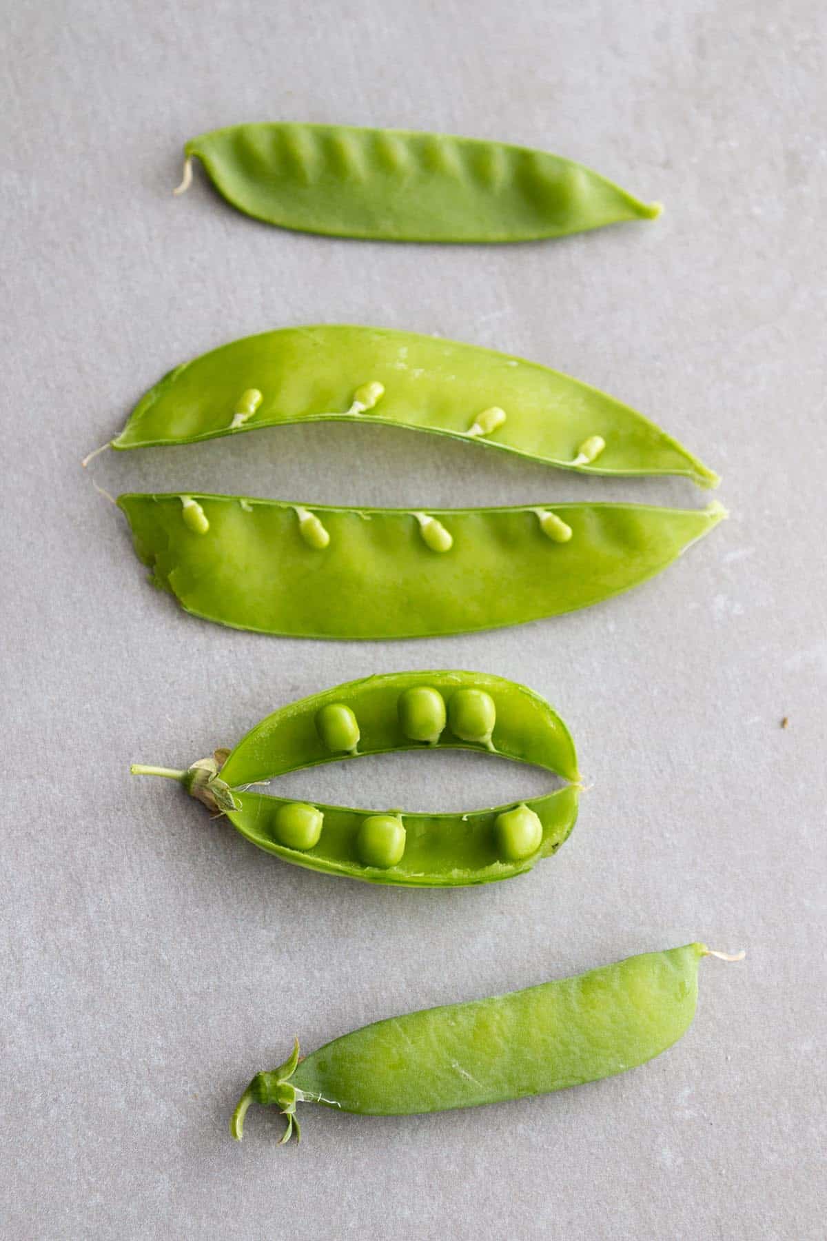Four peas. Two whole and two split open showing the peas inside.
