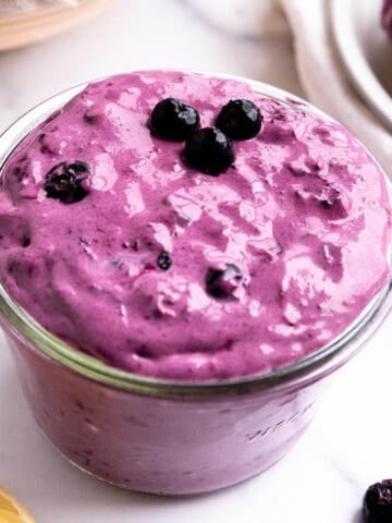 A jar of purple cream cheese with fresh blueberries on top.